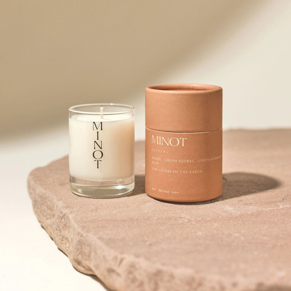 Candle and container with 'MINOT' branding on a stone surface