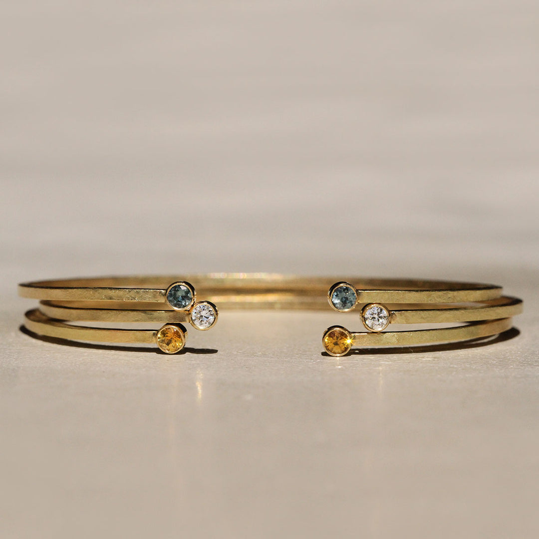 Sophie Hughes Yellow Montana Sapphire Cuff Bracelet in 18k Yellow Gold featuring two 3mm Dark Yellow Montana Sapphire round gemstones, styled with the same cuff in teal Montana Sapphire and Diamond versions.