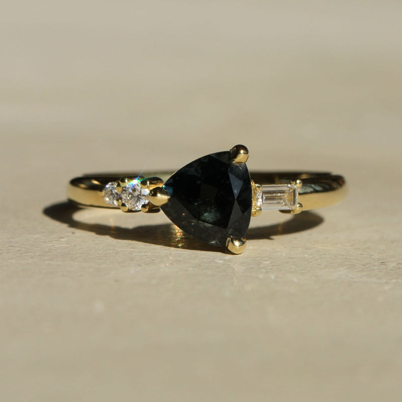 Sophie Hughes Composition Prong Ring in 18K Yellow Gold featuring a 1-ct Dark Teal Trillion Cut Montana Sapphire with 2 round diamonds and 1 baguette diamond