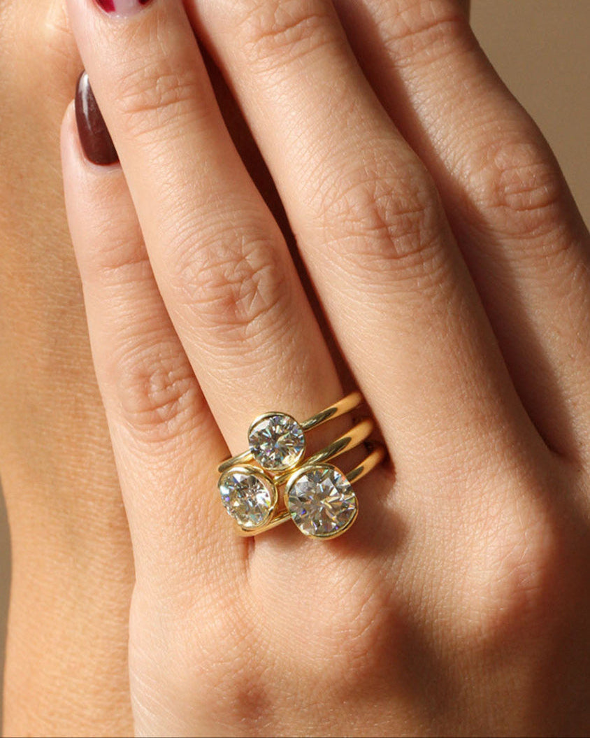 Close-up of a hand wearing two gold rings with gemstones on a neutral background