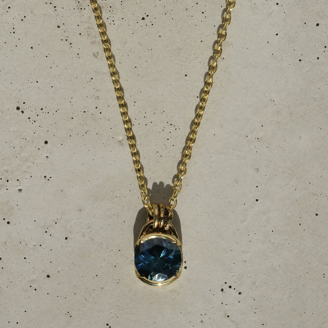 A blue Montana Sapphire necklace set in a yellow gold bezel, with the pendant hanging from a gold chain.