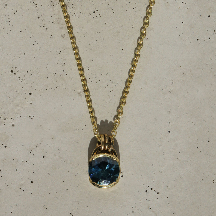 A blue Montana Sapphire necklace set in a yellow gold bezel, with the pendant hanging from a gold chain.