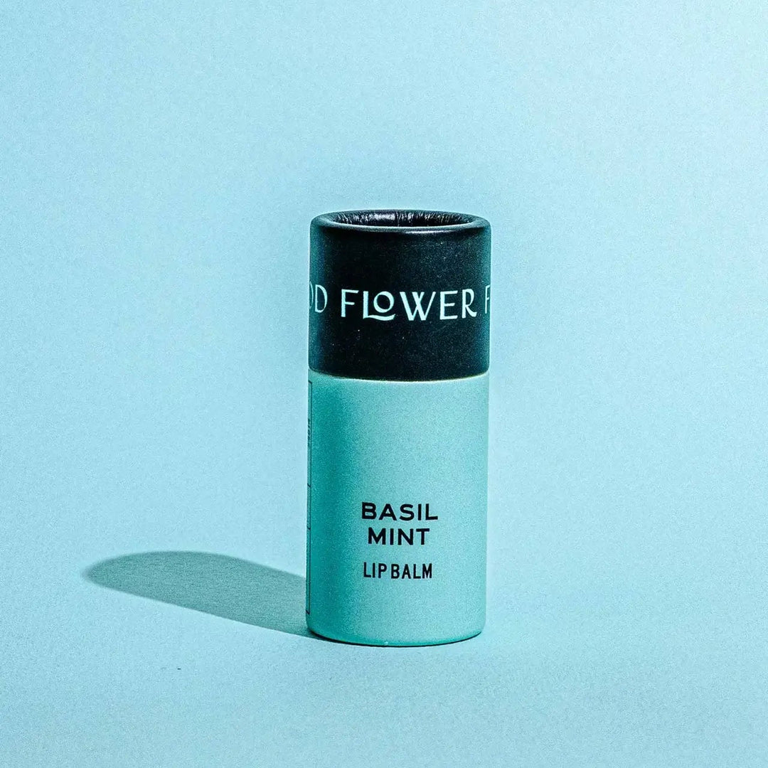 Good Flower Farm Basil Mint Lip balm container on a blue background