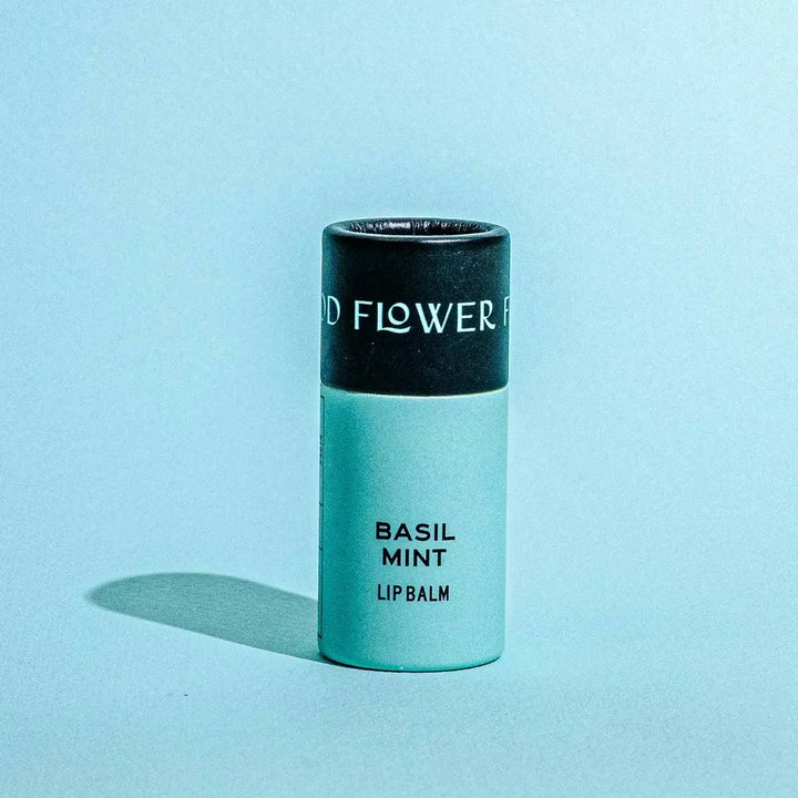 Good Flower Farm Basil Mint Lip balm container on a blue background