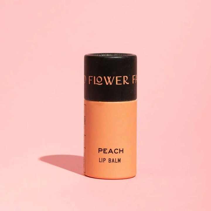 Good Flower Farm Peach Lip balm container on a pink background