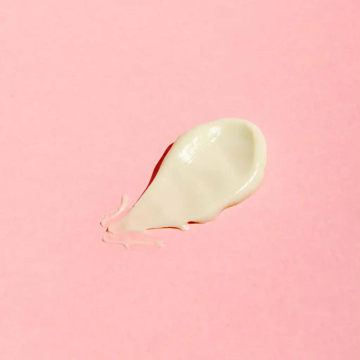 Smear of Good Flower Farm moisturizing Rose Geranium face cream on a pink background