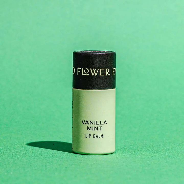 Good Flower Farm Vanilla Mint Lip balm container on a green background
