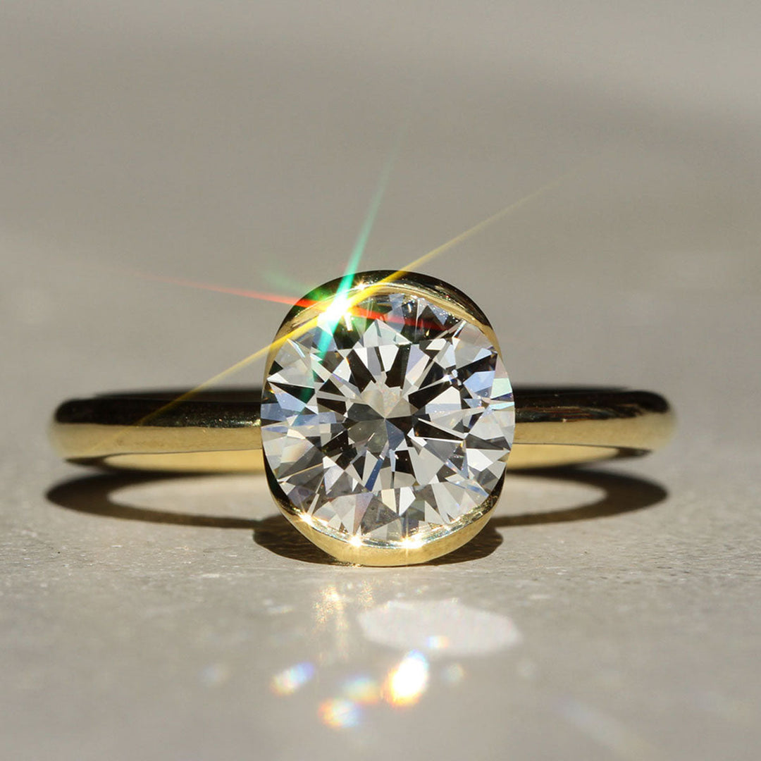 A close-up image of a round diamond ring with a gold band, showcasing the diamond's brilliance and the sleek design of the ring.