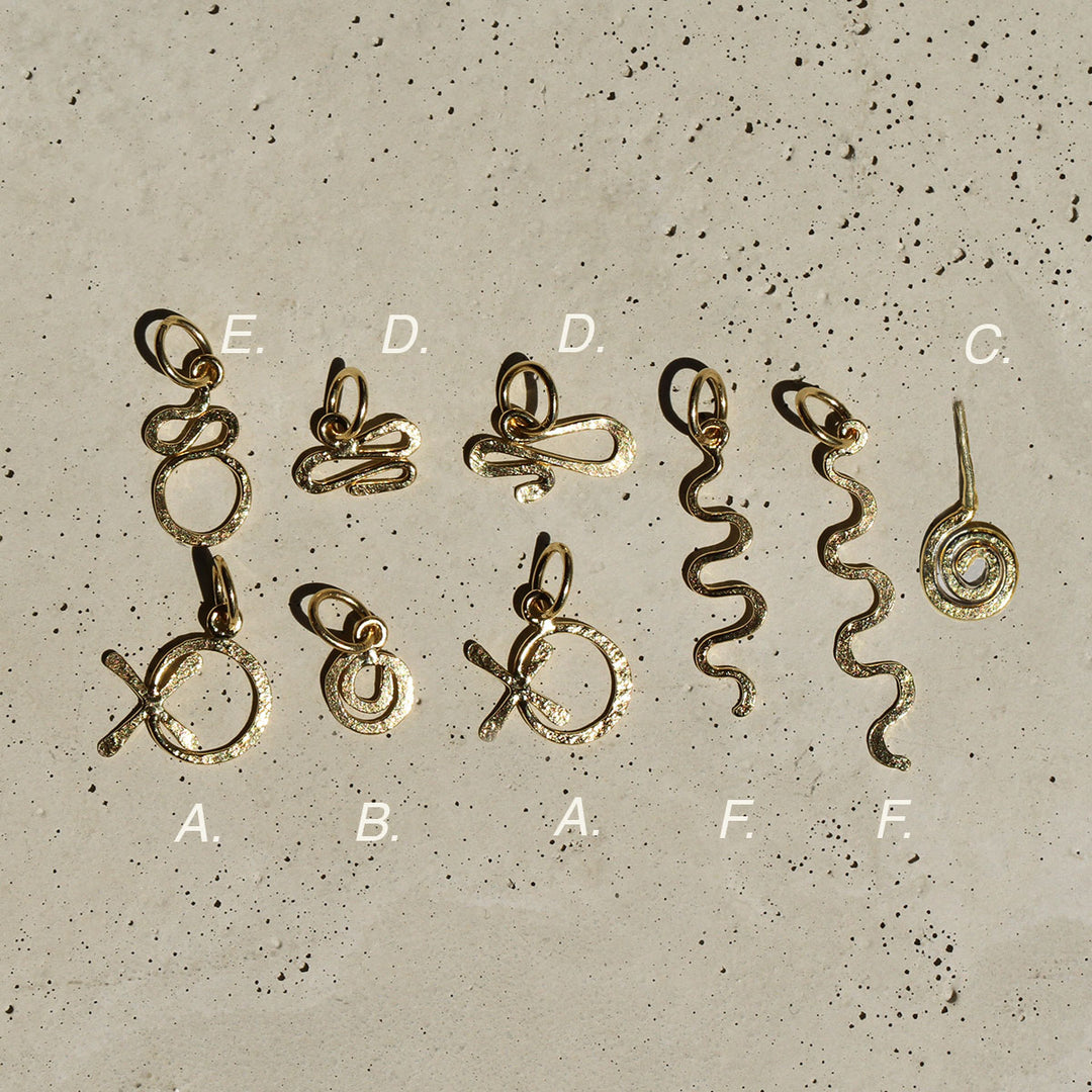 A collection of hand-formed gold charms with a hammered texture, laid out on a concrete surface.