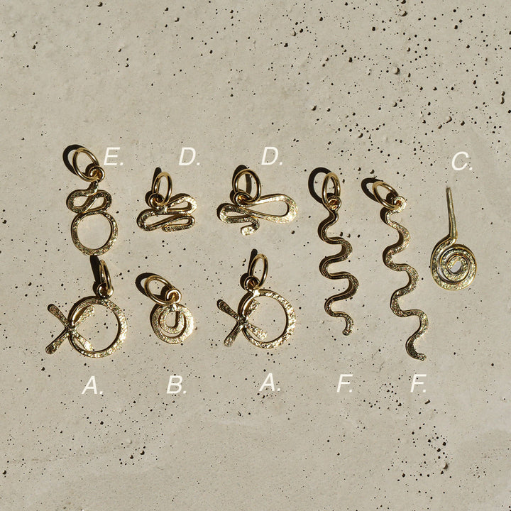 A collection of hand-formed gold charms with a hammered texture, laid out on a concrete surface.