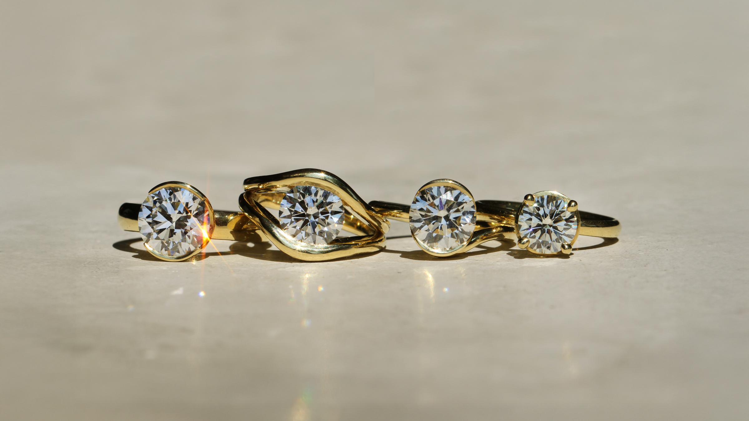 Set of four 18k Yellow Gold rings with round diamond stones on a beige background
