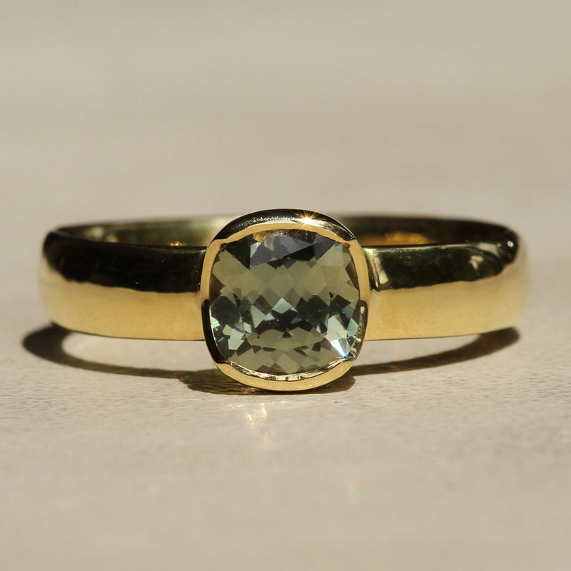 A cushion cut Montana Sapphire ring with a yellow gold band and bezel setting.