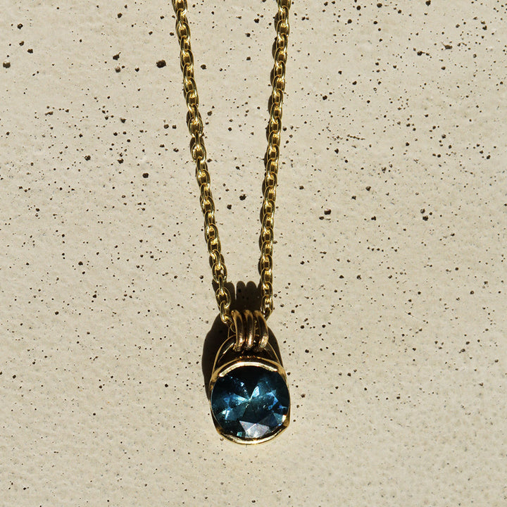 A blue Montana Sapphire necklace set in a yellow gold bezel, with the pendant hanging from a gold chain.
