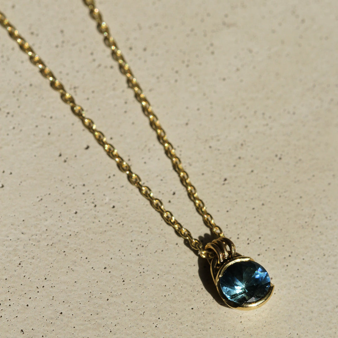 A blue Montana Sapphire necklace set in a yellow gold bezel, with the pendant hanging from a gold chain.
