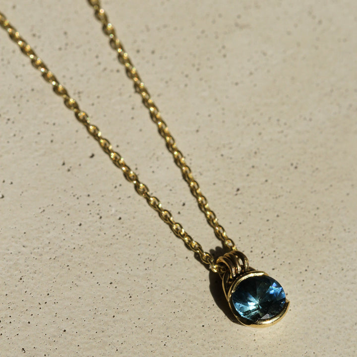 A blue Montana Sapphire necklace set in a yellow gold bezel, with the pendant hanging from a gold chain.