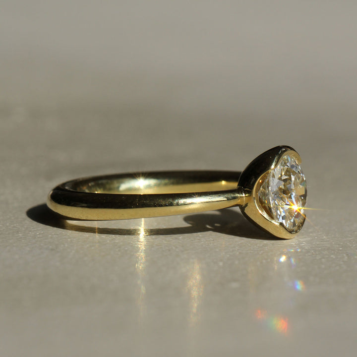 An antique Old European cut solitaire diamond ring with 18k Yellow Gold partial bezel with a tapered band on a neutral background from the side