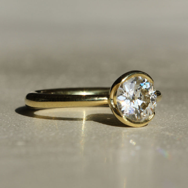 An antique Old European cut solitaire diamond ring with 18k Yellow Gold partial bezel with a tapered band on a neutral background at a slight angle