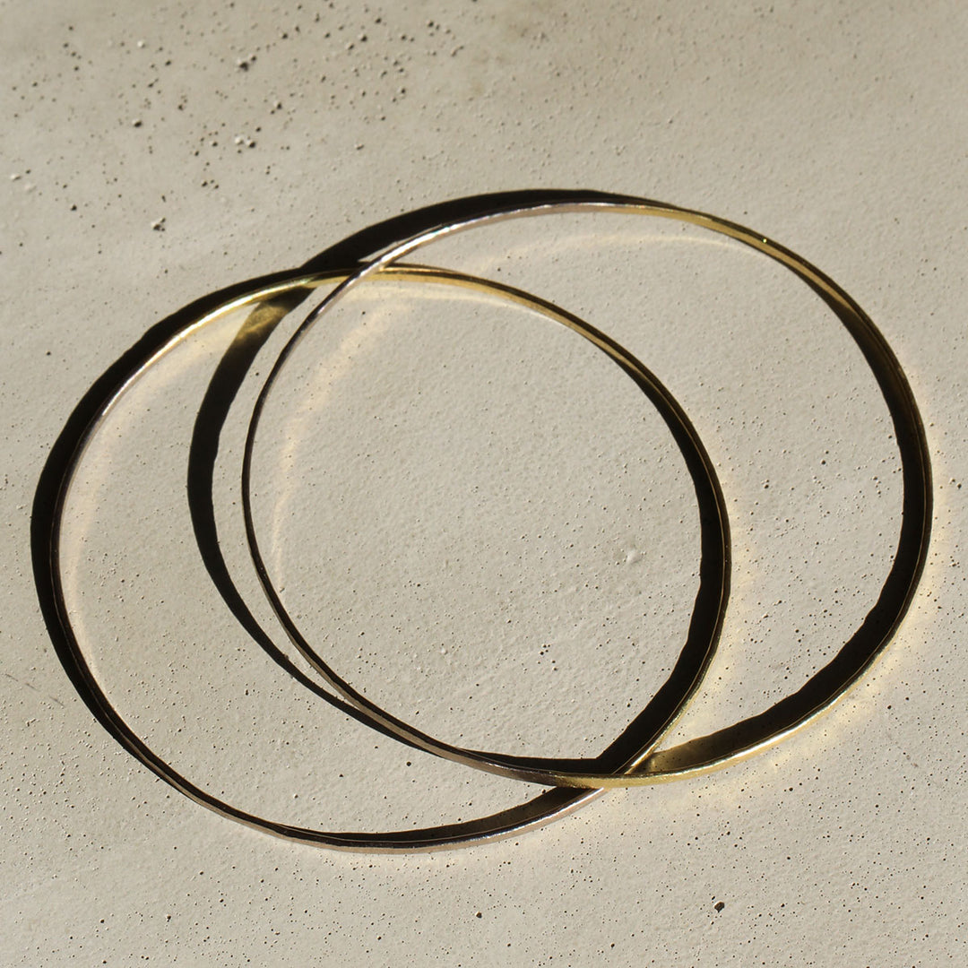 Two bangles on a beige background, one with a 18k yellow gold appearance and the other with a 18k grey gold appearance.