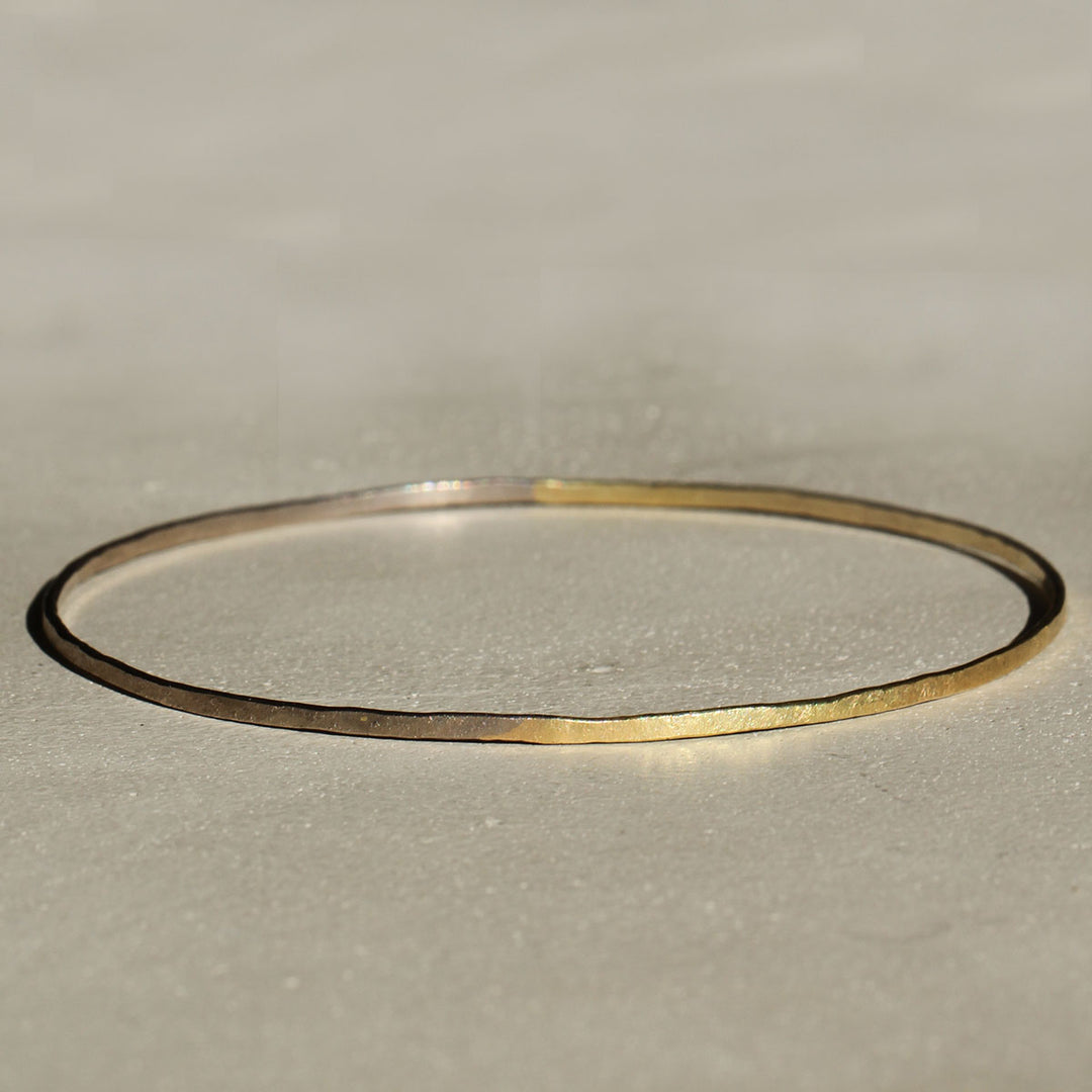 Two bangles on a beige background, one with a 18k yellow gold appearance and the other with a 18k grey gold appearance.