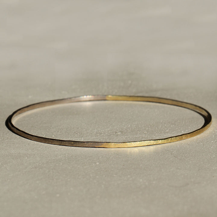 Two bangles on a beige background, one with a 18k yellow gold appearance and the other with a 18k grey gold appearance.