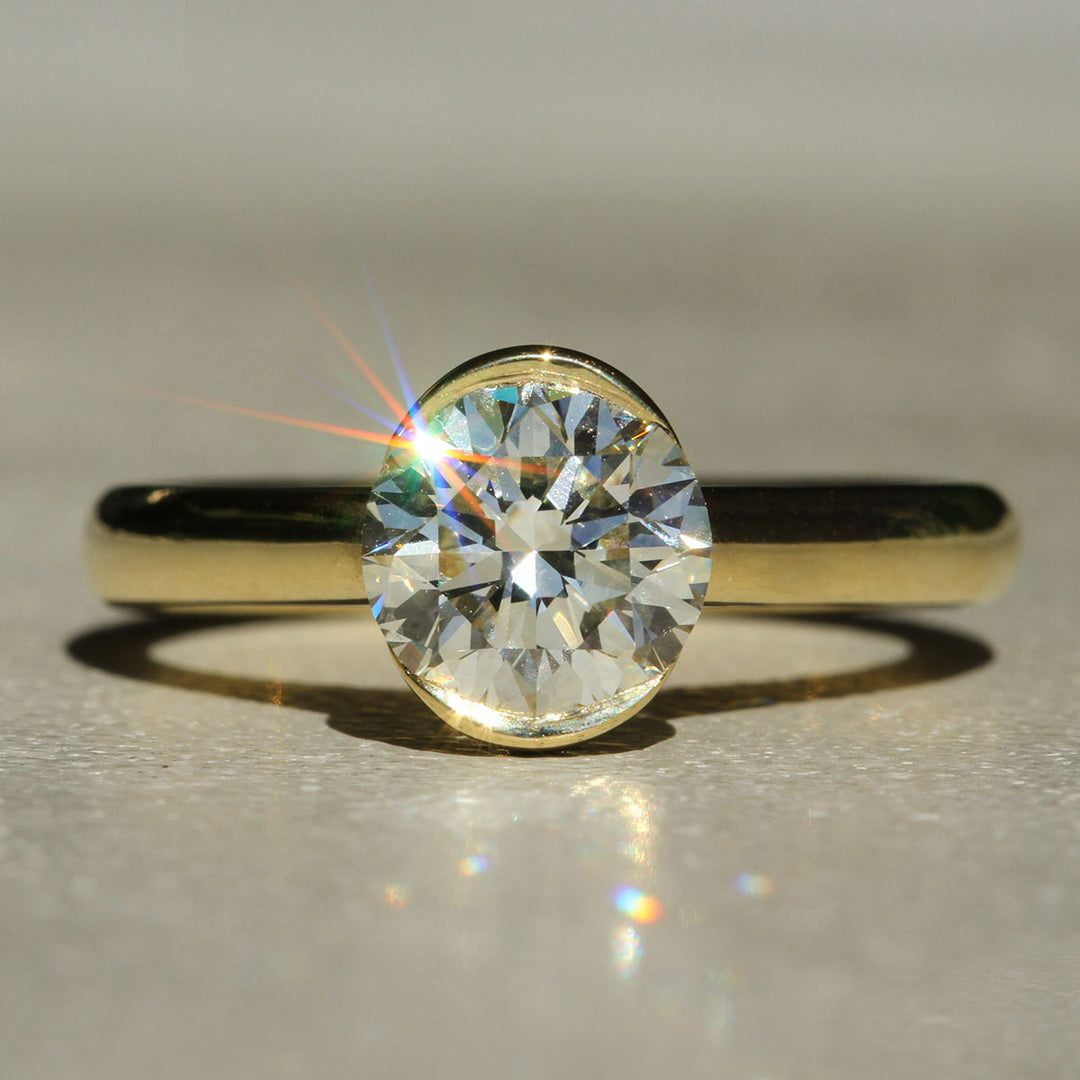 A close-up image of a diamond ring with a gold bezel set, showing the diamond's brilliance and the gold band.