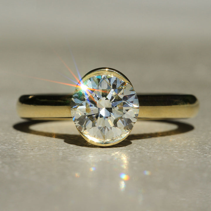 A close-up image of a diamond ring with a gold bezel set, showing the diamond's brilliance and the gold band.