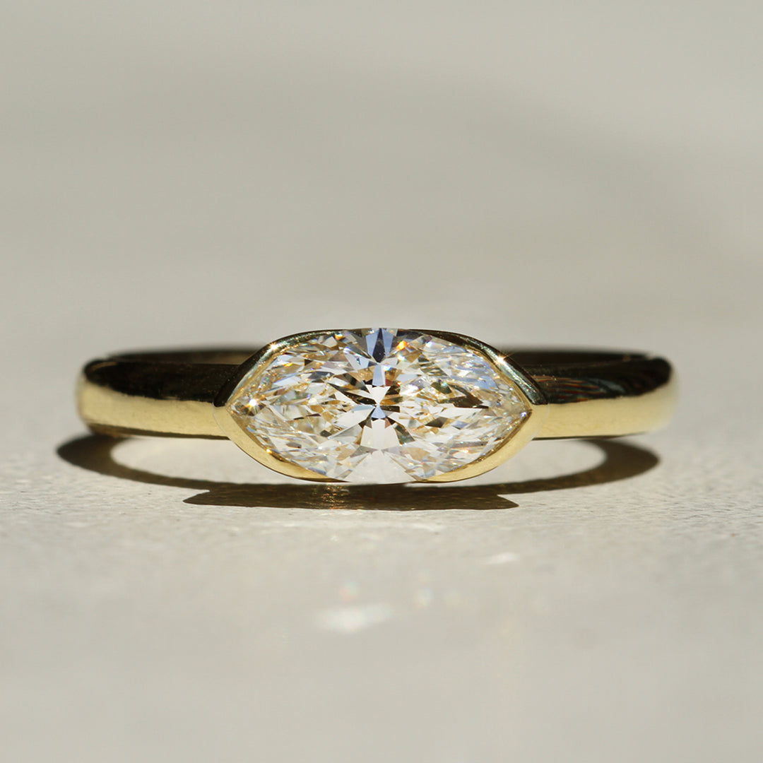 A gold marquise diamond ring with a bezel setting, displayed on a white background.