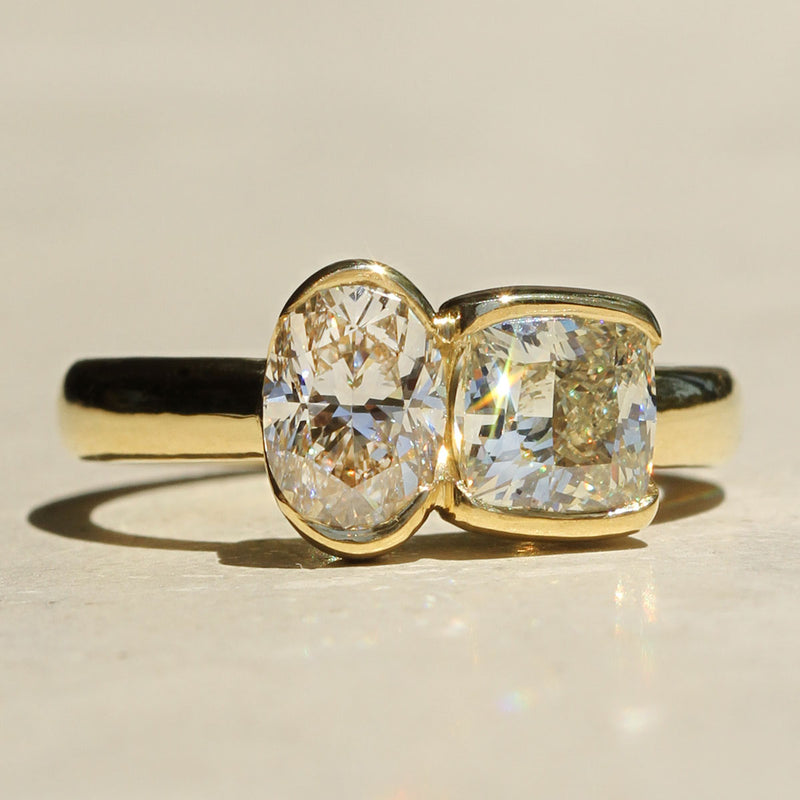 Sophie Hughes Poppy Bezel Toi et Moi Ring in 18K Yellow Gold featuring a 1-carat Cushion Cut Diamond and a 1-carat Oval Cut Diamond
