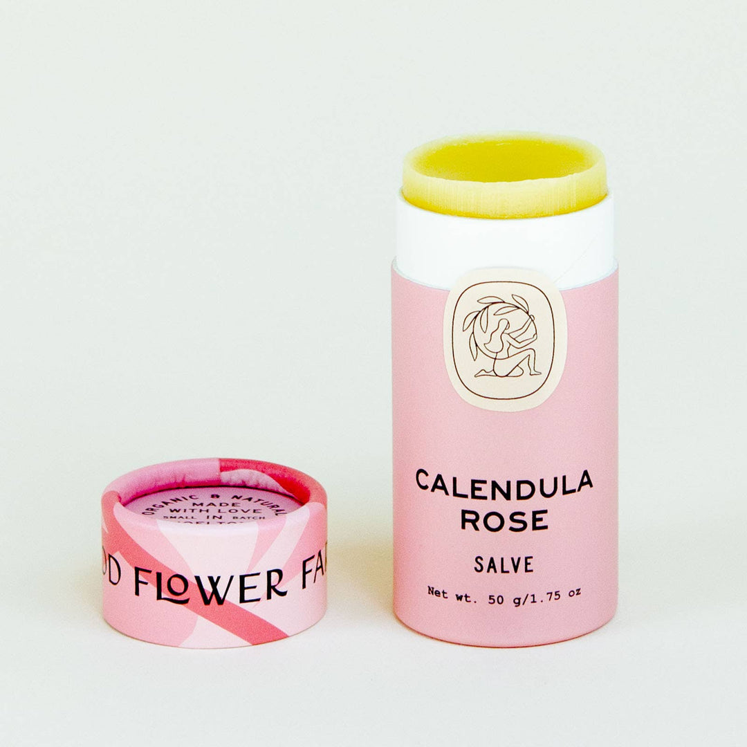 A pink and white paperboard tube labeled 'Calendula Rose Salve' with a yellow cap, next to its open lid revealing the product inside.