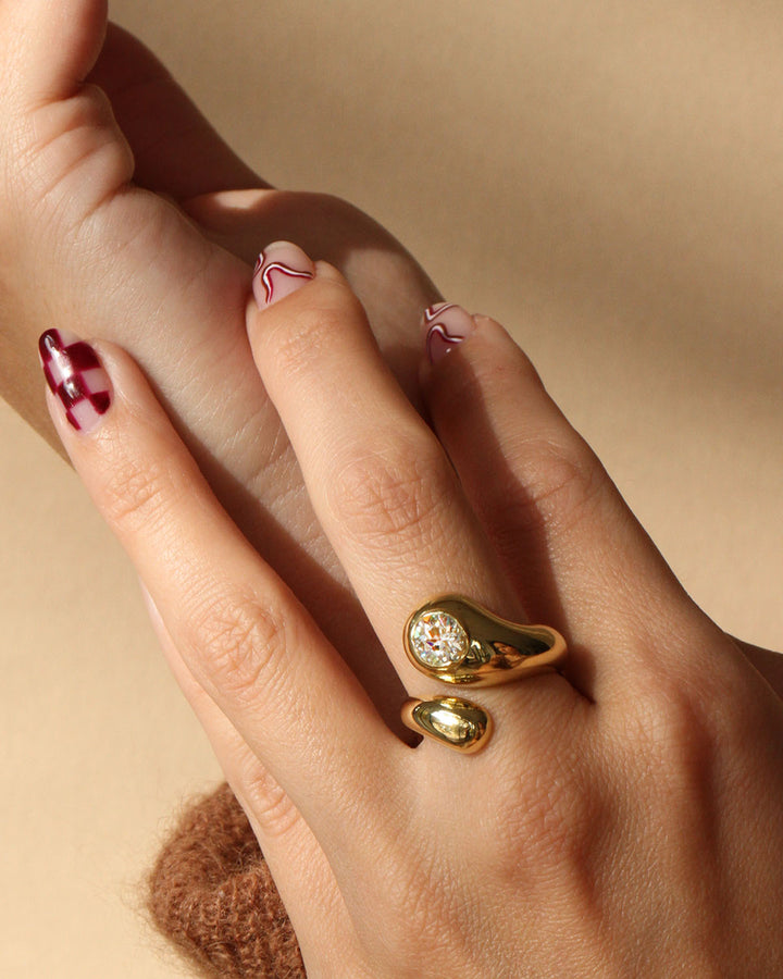 A hand wearing an 18k yellow gold bypass ring with an antique cut Old European diamond set in the center, creating a bold and luxurious look.