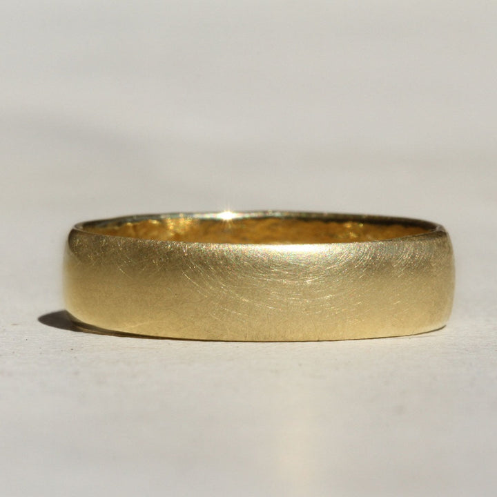 A wide half round gold band with a brushed finish, displayed on a light background.