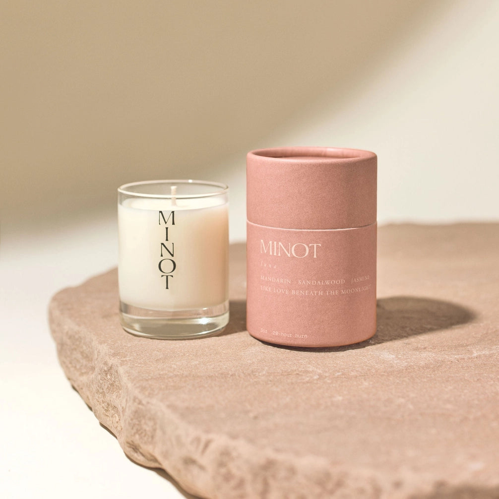 Candle and pink container with 'MINOT' branding on a beige surface.
