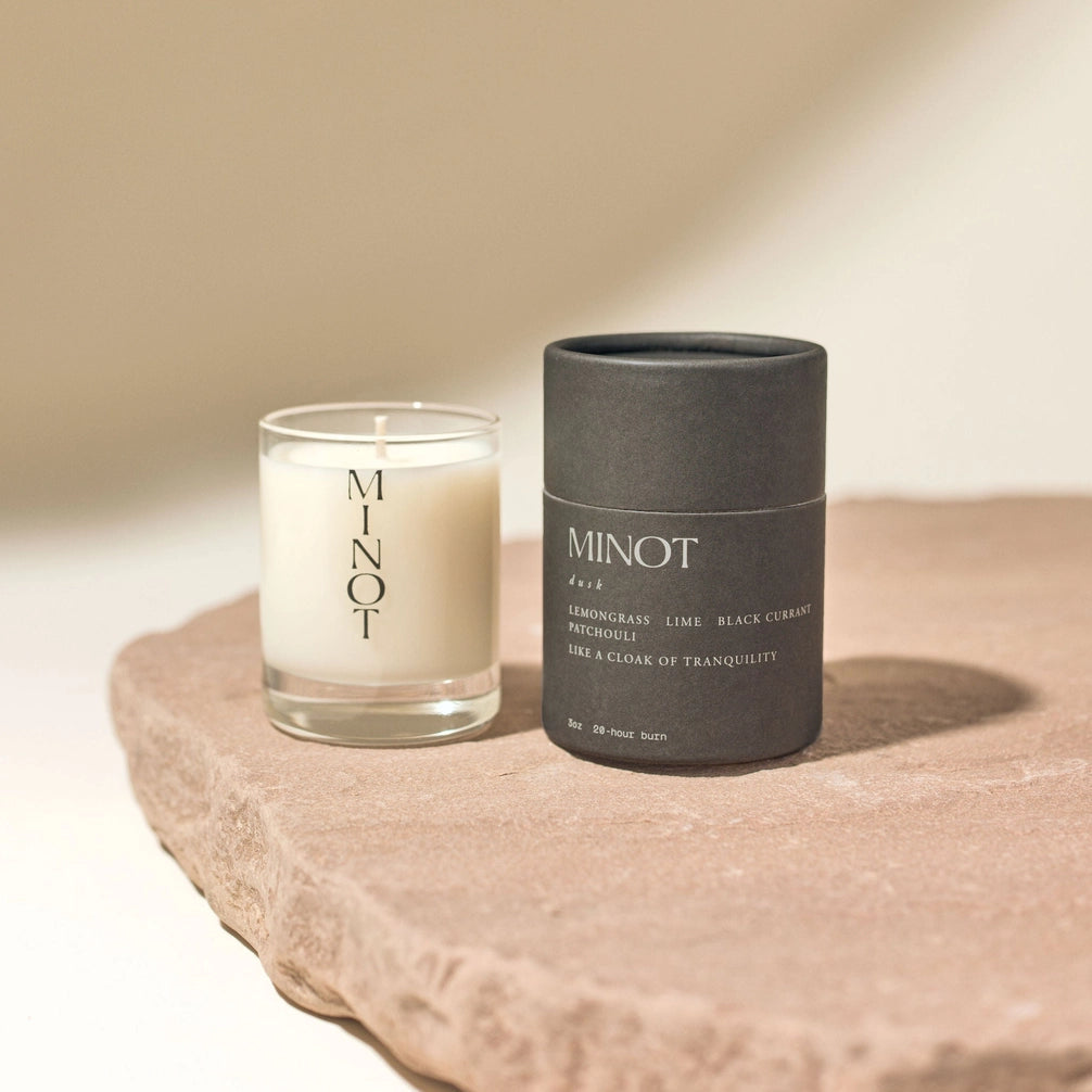 Two candles labeled 'MINOT' on a stone surface with a neutral background