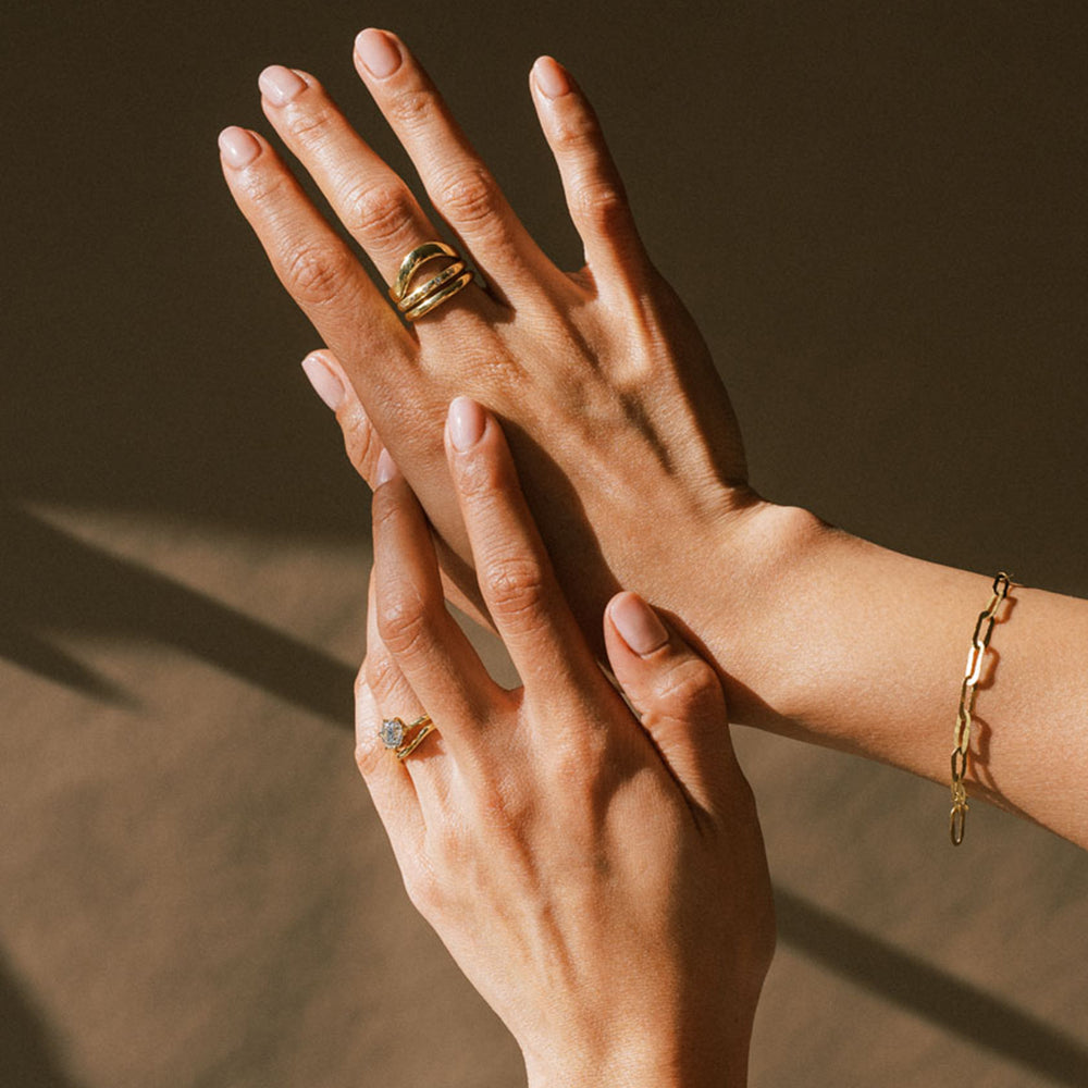 A person's hands wearing a thin link chain bracelet with a hammered texture and a hook clasp.