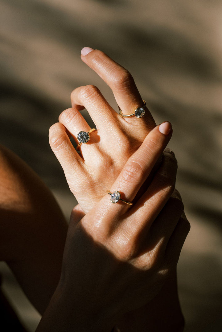 A hand wearing two antique-cut Old European white diamond solitaire rings with a partial bezel setting, 18k Yellow Gold tapered band on a neutral background.
