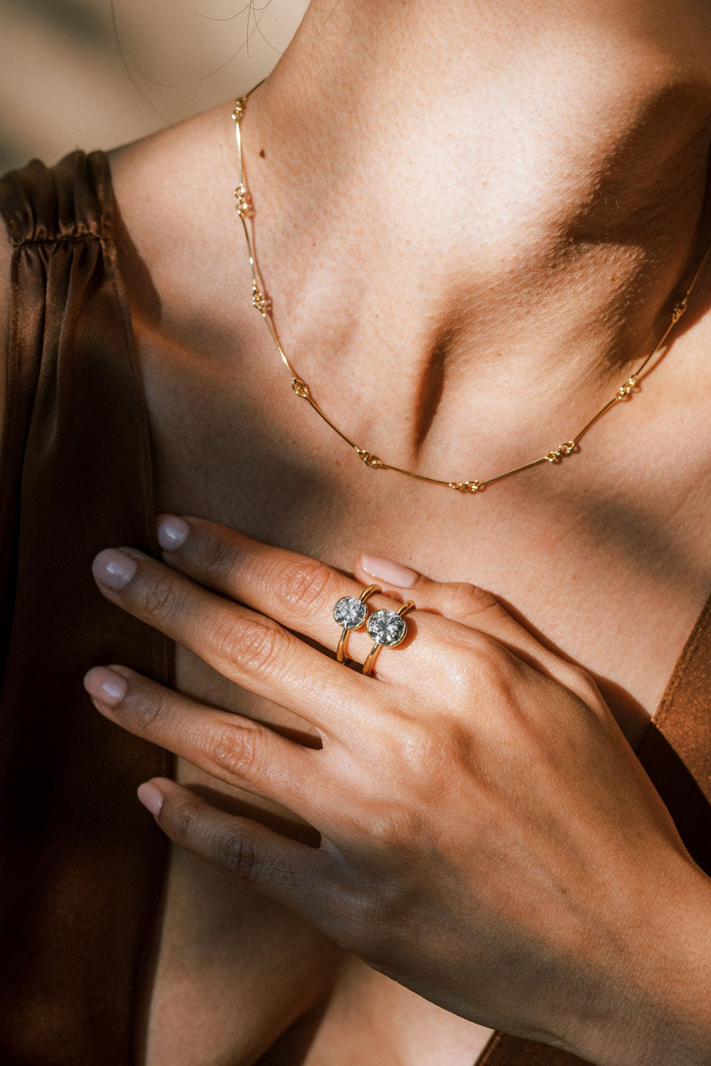 A hand wearing two antique-cut Old European white diamond solitaire rings with a partial bezel setting, 18k Yellow Gold tapered band on a neutral background.