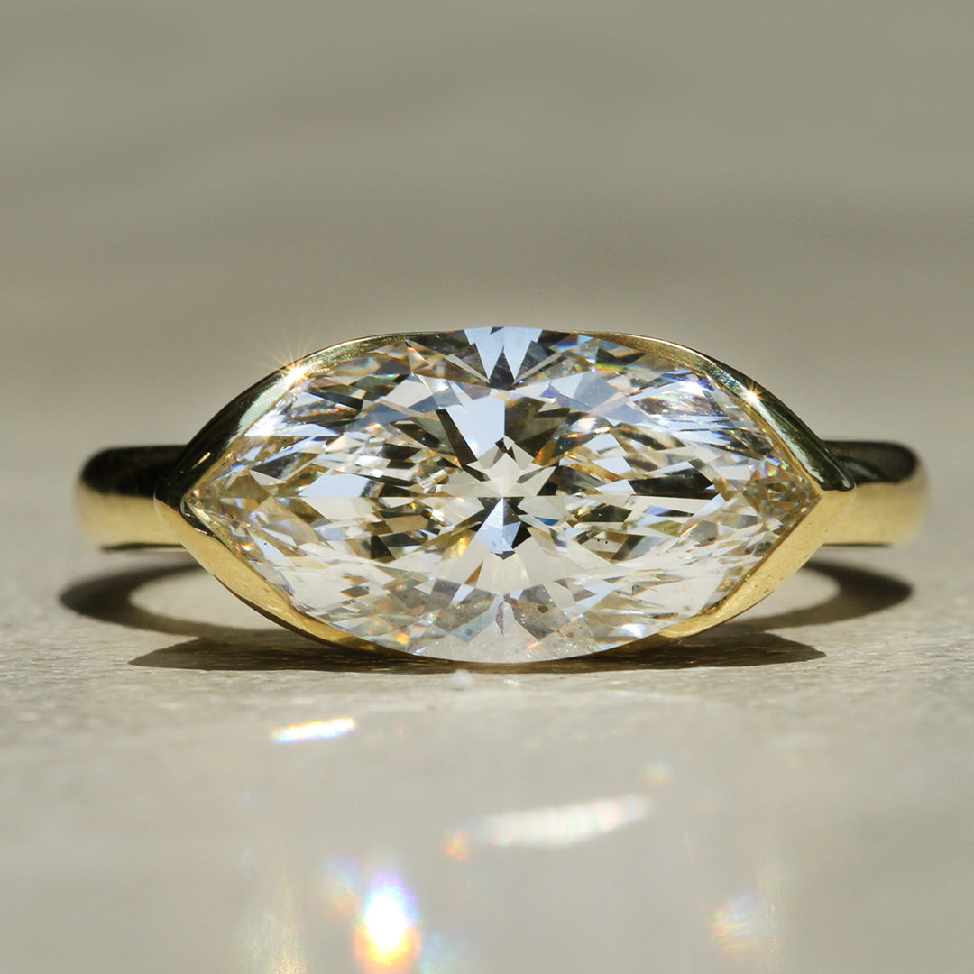 18k Yellow Gold solitaire ring with a large Marquise cut white diamond on a neutral background