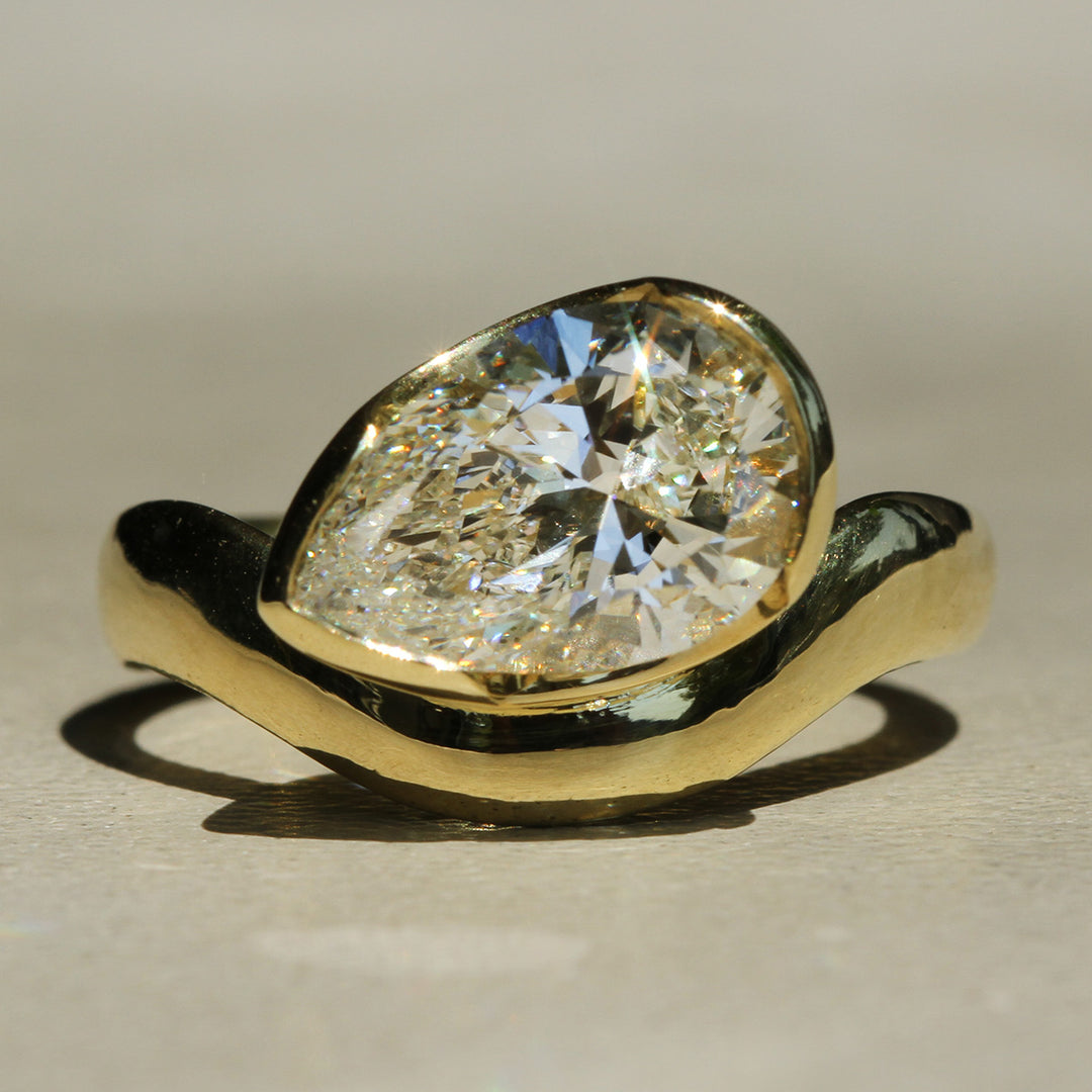 18k Yellow Gold ring with a large Pear shaped diamond set in a partial bezel offset on a curved band.