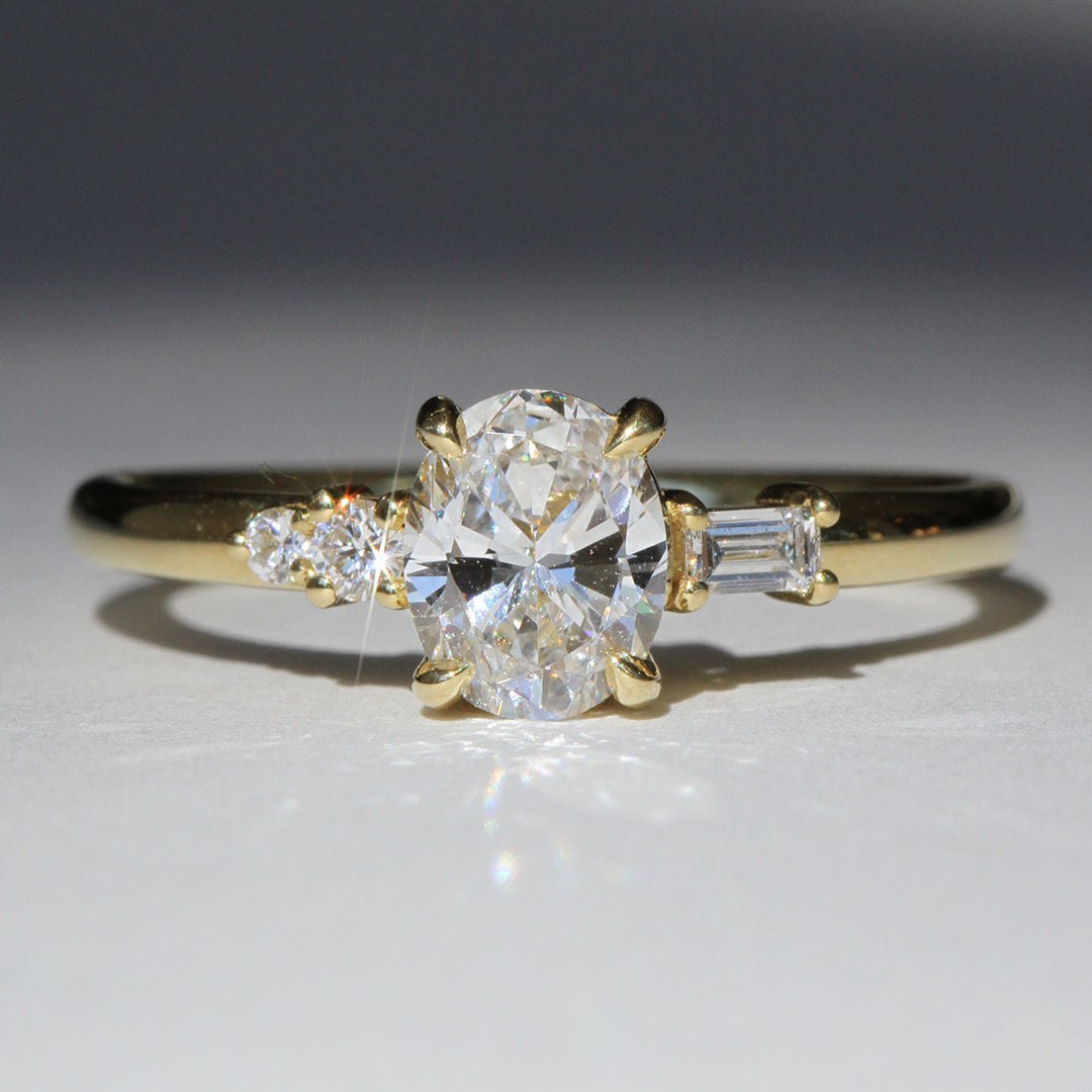 A reclaimed oval cut diamond ring with smaller stones set in a yellow gold band, photographed on a white background.