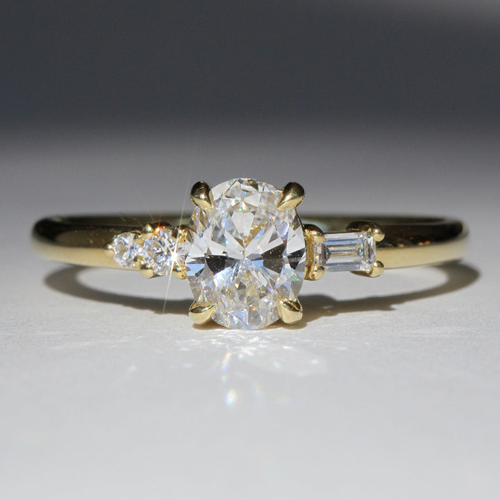 A reclaimed oval cut diamond ring with smaller stones set in a yellow gold band, photographed on a white background.