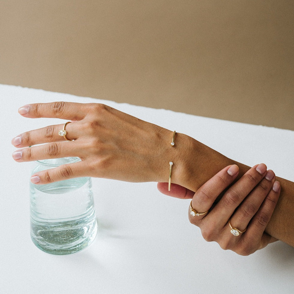 A person's wrist wearing a yellow gold cuff bracelet with a lightly hammered texture and two bezel-set diamonds.